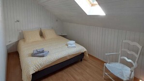Une chambre avec un plafond en pente, un puits de lumière, un lit recouvert d’une couvre-lit à motifs, une chaise et un plancher en bois.