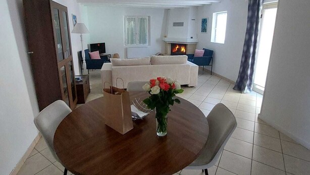 Un coin repas avec une table ronde, des chaises, un vase de fleurs et une cheminée en arrière-plan.