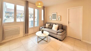 Un salon moderne avec un canapé gris, une table basse ronde et une grande fenêtre avec des rideaux.