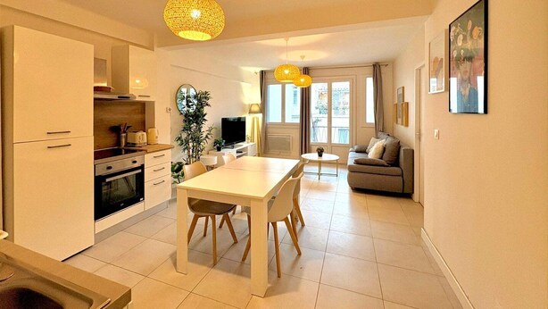 Une cuisine moderne avec des meubles blancs, une table à manger avec des chaises, un canapé et un téléviseur.
