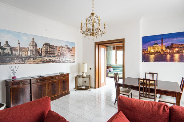 A hotel room with a dining area, a chandelier, a large window, and a painting of a cityscape. - Happio Apartment Appio Latino (Roma)
