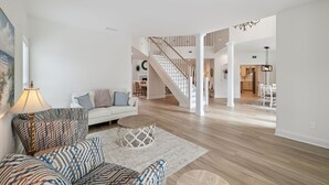 Ein geräumiges Wohnzimmer mit einem weißen Sofa, gemusterten Sesseln und einem runden Couchtisch. Eine Treppe führt auf eine Erschließung.