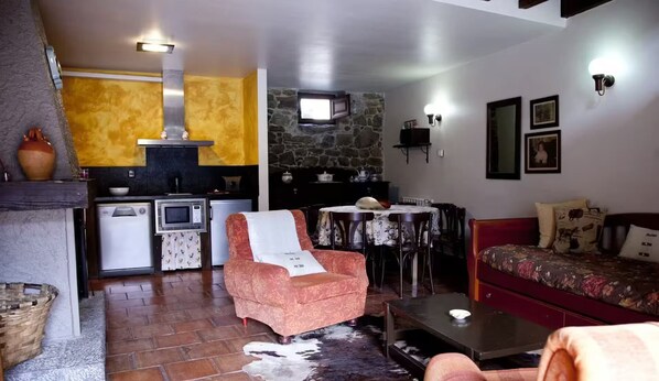A cozy living room with a sofa, a chair, a small table, and a kitchen area with a stove and microwave.