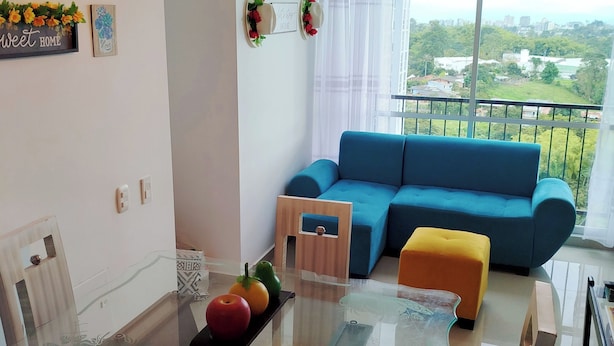 Una sala de estar moderna con un sofá azul, una mesa de comedor de vidrio y un balcón con vistas.
