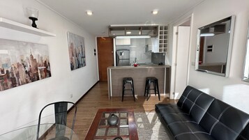 Una sala moderna con un sofá de cuero negro, una mesa de centro de vidrio y un cuadro de un paisaje urbano en la pared.