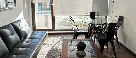 A modern living room with a leather sofa, a glass coffee table, and a dining area with chairs.