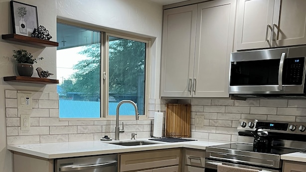 A modern kitchen with stainless steel appliances, a window, and a view of trees. - Centrally located Tucson home, renovated 2 bedroom/1 bath home. (Tucson)
