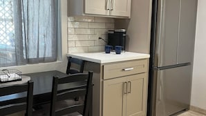 A modern kitchen with light-colored cabinets, a stainless steel refrigerator, a coffee maker, and a dining table with chairs. - Centrally located Tucson home, renovated 2 bedroom/1 bath home. (Tucson)