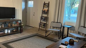 A living room with a television, bookshelves, a coffee table, and a window with curtains. - Centrally located Tucson home, renovated 2 bedroom/1 bath home. (Tucson)
