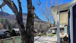 Une terrasse en bois avec un grand arbre, un espace abrité et une vue sur une montagne et des bâtiments en arrière-plan.