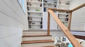 Un escalier avec des marches en bois et une rampe en bois, menant à une pièce où se trouvent une table à manger et des chaises.