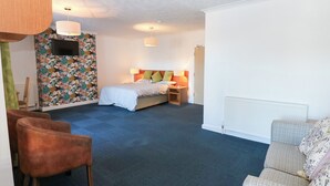 Habitación de hotel con cama, televisor montado en la pared, escritorio con lámpara y una silla.