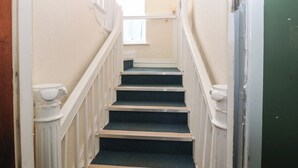 Una escalera estrecha con barandillas blancas y una puerta verde al final.