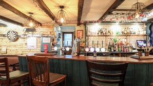 Eine Bar mit Holzsesseln, einer Dartscheibe und einer Auswahl an Flaschen in Regalen.