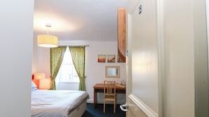 Ein Schlafzimmer mit einem Bett, einem Schreibtisch und einem Stuhl. Es gibt ein Fenster mit Vorhängen, eine Lampe und Wandbilder.
