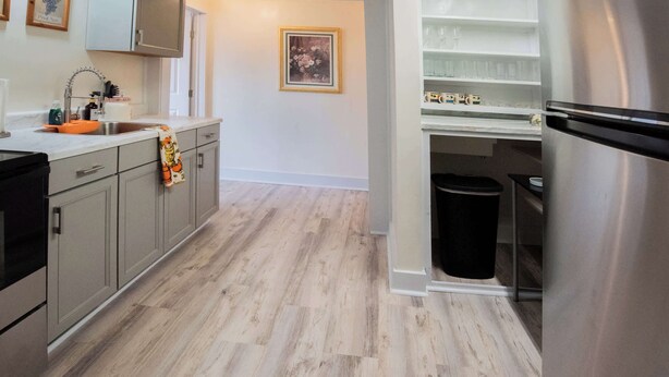 A modern kitchen with grey cabinets, a stainless steel refrigerator, and a wooden floor. - Mariposa Coral Home for 4 (Kerrville)