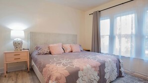 A bedroom with a bed, a bedside table, a lamp, and a window with curtains. - Mariposa Coral Home for 4 (Kerrville)