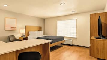 A compact hotel room with a bed, desk, chair, and a television on a wooden cabinet.