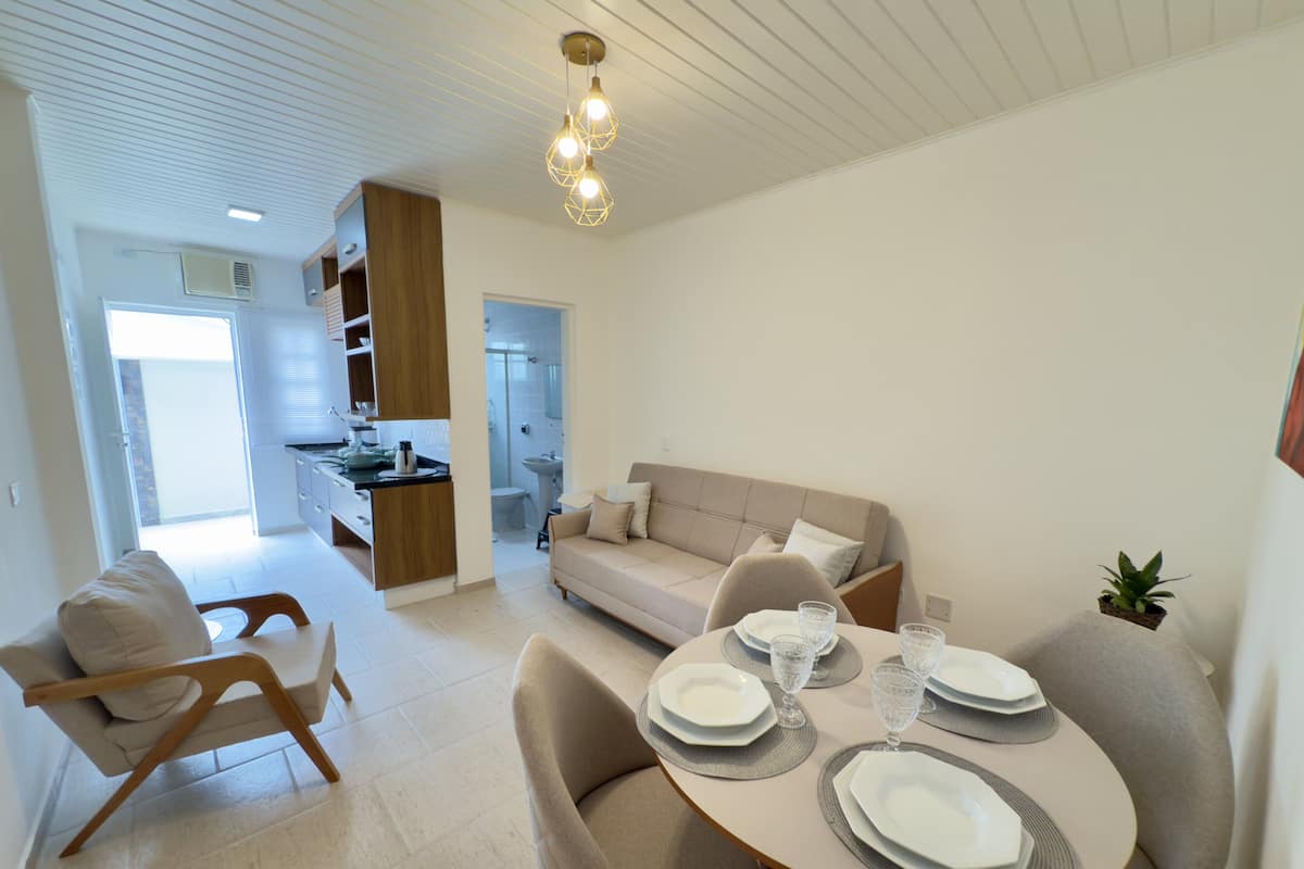 A modern living room with a dining area, a sofa, and a kitchen in the background.