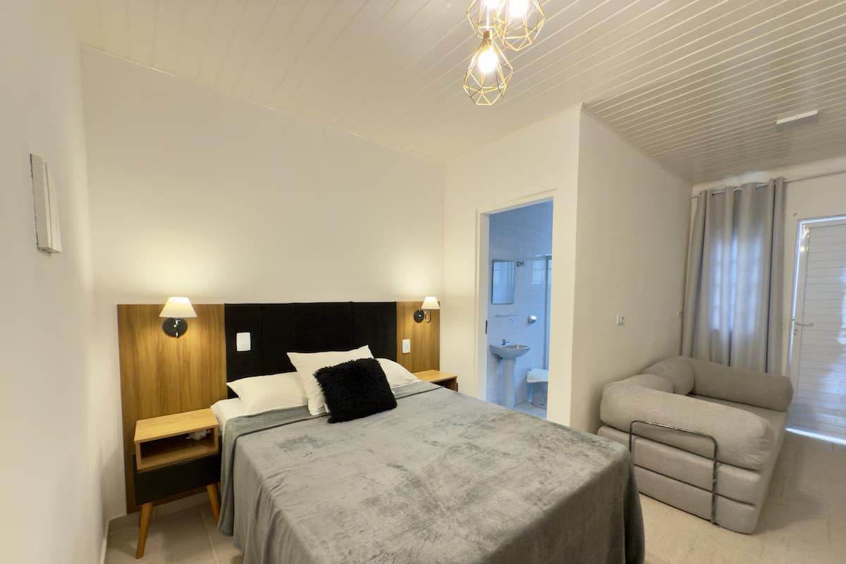 A bedroom with a bed, bedside tables, a nightstand, a sofa, and a bathroom visible through an open door.