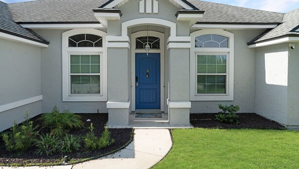 Una casa de dos pisos con puerta azul, detalles blancos y un pequeño porche con felpudo.