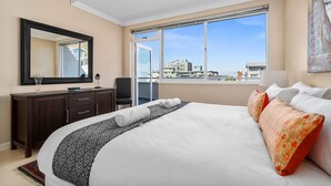 Une chambre d’hôtel avec un grand lit, une commode en bois foncé, un miroir et une fenêtre donnant sur la ville.