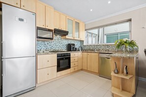 Eine moderne Küche mit Holzschränken, einem Edelstahlkühlschrank, einer Mikrowelle, einem Backofen und einem Geschirrspüler.