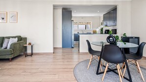 A modern living room with a green sofa, a small side table, and a dining area with a round table and black chairs.