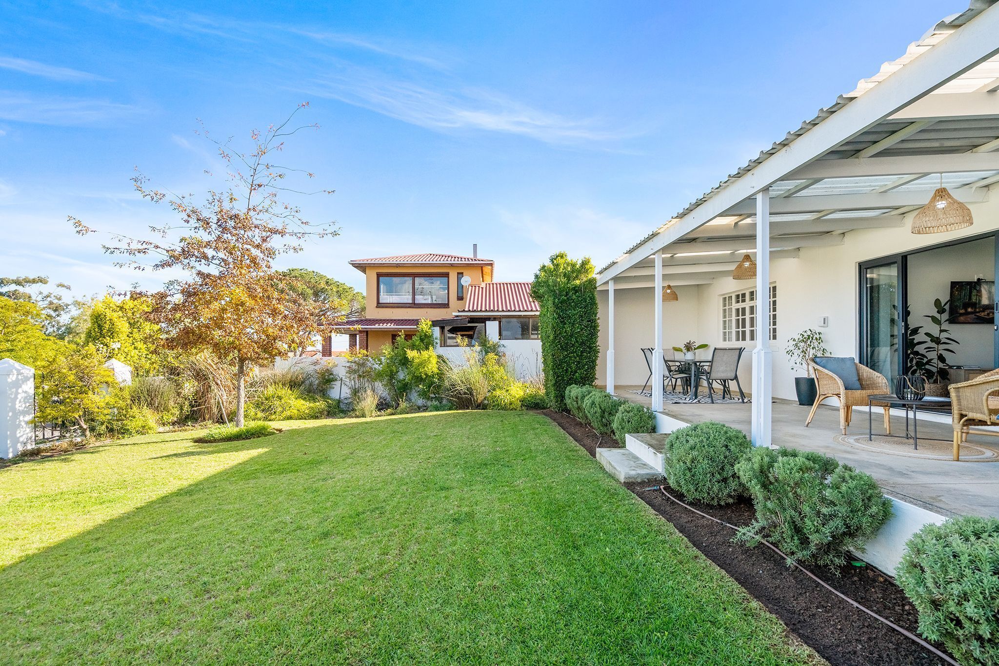 A modern house with a well-maintained lawn, a patio with furniture, and a large window overlooking the garden.