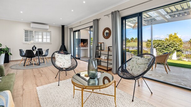 A spacious living area with a glass door leading to a balcony, a dining table with chairs, and a seating area with a round table and chairs.