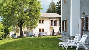Een gebouw met balkon, boom en een gazon met lounge stoelen.
