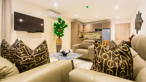 A modern living room with a flat-screen TV, a coffee table with decorative items, and a sofa with patterned cushions. - Comfy One Bedroom Apartment @ The Bantree (Accra)