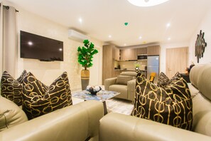 A modern living room with a flat-screen TV, a coffee table with decorative items, and a sofa with patterned cushions. - Comfy One Bedroom Apartment @ The Bantree (Accra)