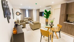 A modern living room with a sofa, coffee table, and a dining area with a glass table and chairs. - Comfy One Bedroom Apartment @ The Bantree (Accra)