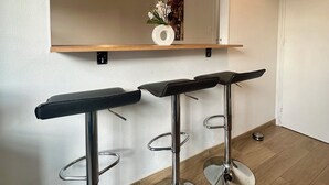 Una cocina moderna con encimera de madera, dos taburetes de bar, una lámpara colgante y un reloj fijado a la pared.