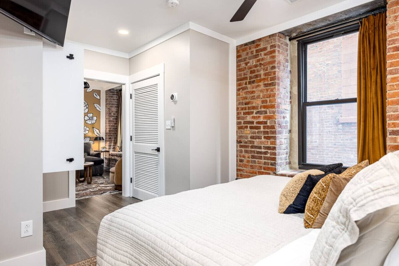 Une chambre avec un grand lit, un mur décoratif en briques, une fenêtre avec des rideaux et une porte donnant sur une autre pièce.