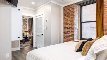 Une chambre avec un grand lit, un mur décoratif en briques, une fenêtre avec des rideaux et une porte donnant sur une autre pièce.