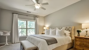 A bedroom with a large bed, a ceiling fan, a window with curtains, a bedside table with a lamp, and a bench. - 3-bedroom townhome in adorable Mableton. Close to all the charms of Atlanta. (Mableton)
