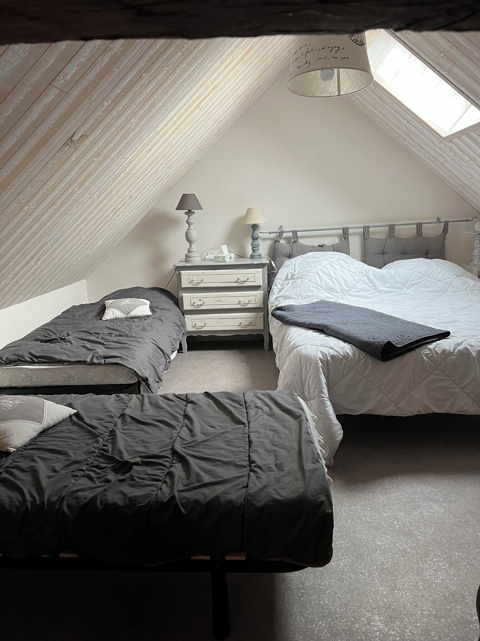 A small, dimly lit attic bedroom with two beds, a nightstand, and a lamp.