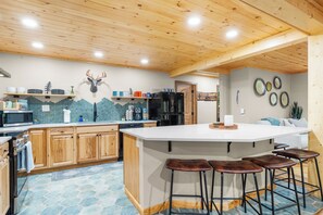 Eine moderne Küche mit Holzschränken, einer zentralen Kochinsel mit Barhocker und einem dekorativen Hirschkopf an der Wand.