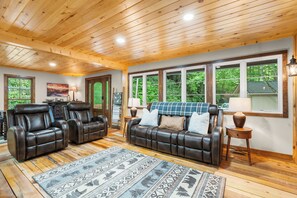 A spacious living room with leather sofas, a patterned rug, and large windows offering a view of the outdoors. - 4 Acres + 4BR Secluded Cabin w Hot Tub & Fire Pit. Next to Blue Ridge Parkway! (Newland)