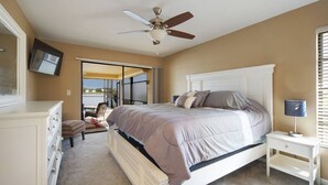 Quarto com cama, mesa de cabeceira, cômoda, ventilador de teto e porta de vidro corrediça que dá para uma varanda.