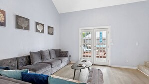 Ein modernes Wohnzimmer mit einem grauen Ecksofa, einem kleinen Couchtisch und einem großen Fenster mit Blick zum Garten.