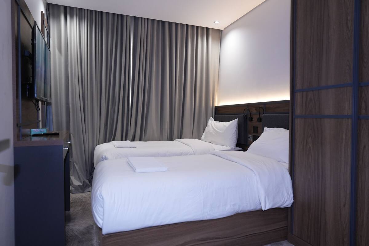 Une chambre d’hôtel avec deux lits, une télévision et une grande fenêtre avec des rideaux.