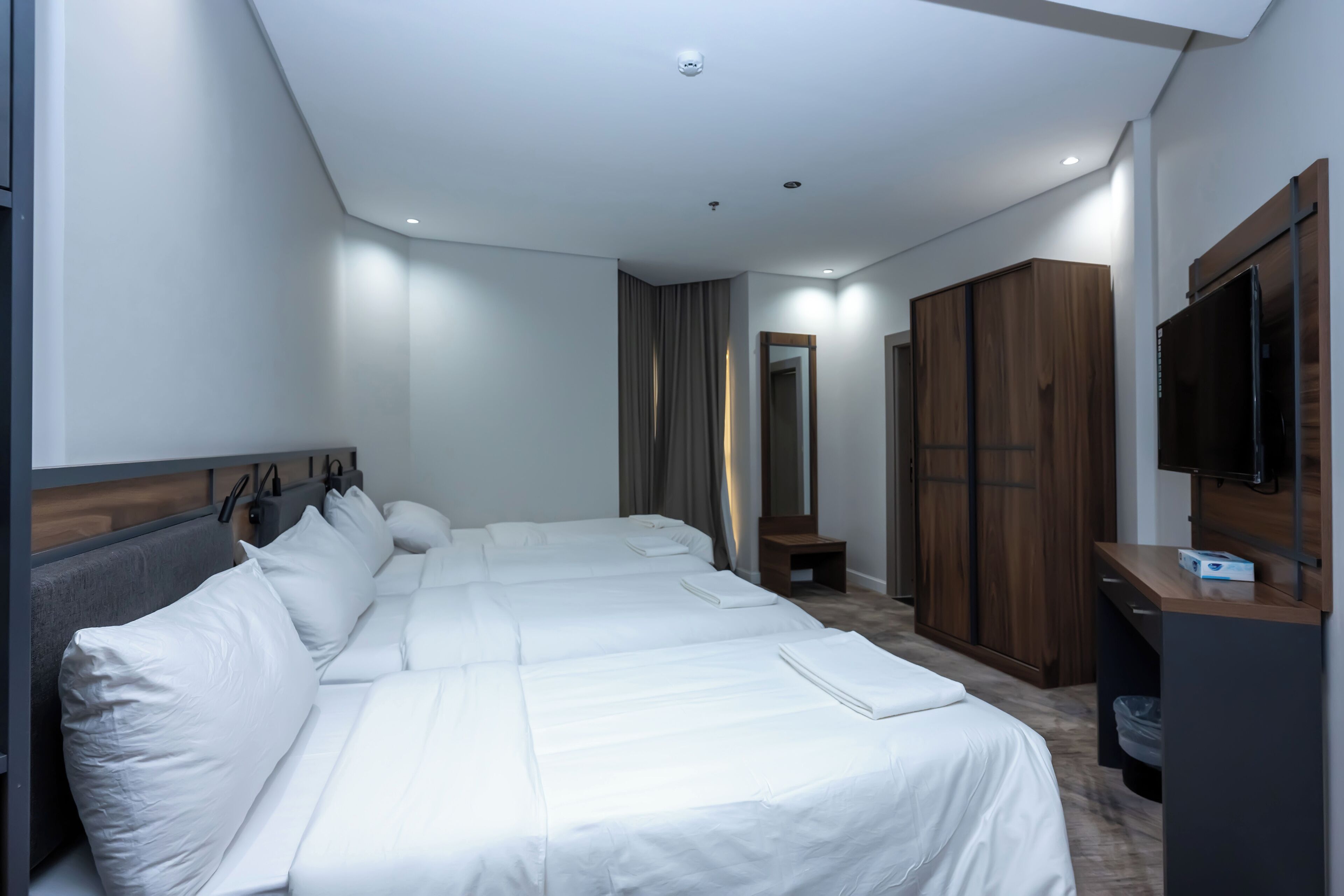 A hotel room with two beds, a wooden wardrobe, a television, and a small table.