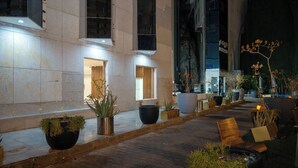 An outdoor area with potted plants, seating, and a building facade with large windows and doors. - Samama Almaqam Hotel - Ajyad ( فندق سمامة المقام ) (Makkah)