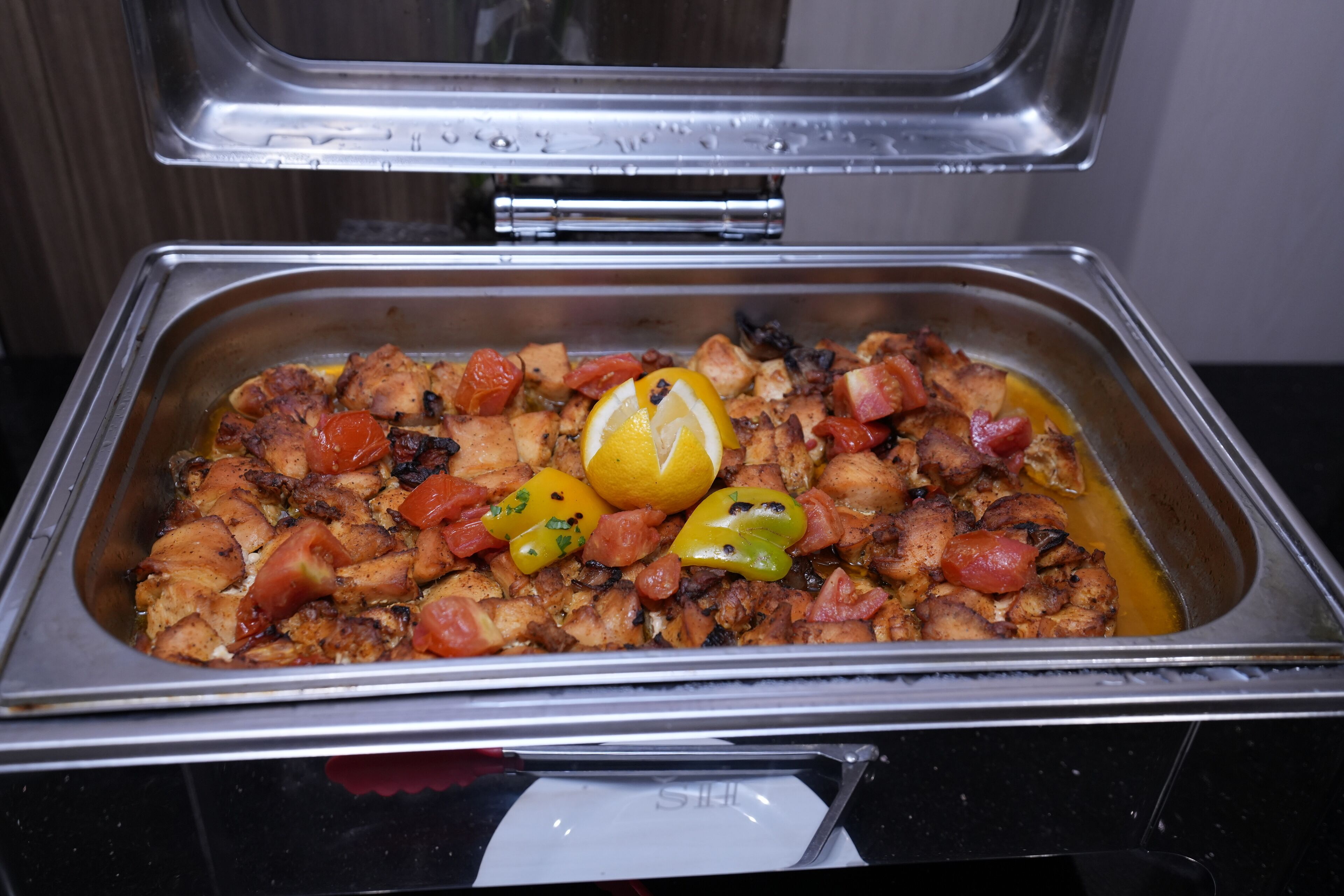 A buffet with a variety of foods including chicken, tomatoes, and bell peppers.
