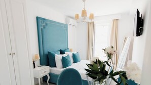 A modern bedroom with a teal headboard, a glass table with a vase of flowers, a teal chair, and a white bedside table with a lamp. - Turquoise studio with AC in beautiful Budva perfect for getaway (Budva)