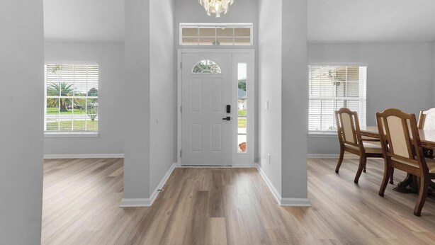 Un pasillo con una puerta blanca, suelo de madera y una zona de comedor con una mesa y sillas.