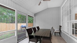 Un patio cubierto con mesa y sillas, ventanas amplias y un ventilador de techo.